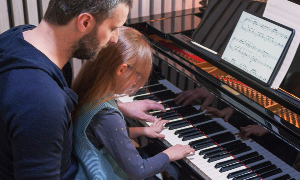 Parent helping child at piano